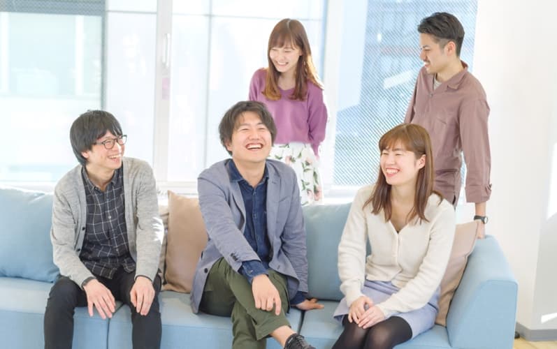 社員の写真。男性3名女性2名がにこやかに語らっている。